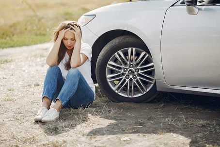 a person sitting next to their car looing stressed after an accident.