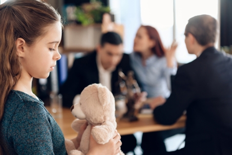 a child holding a teddy bear, in front of her fighting parents.